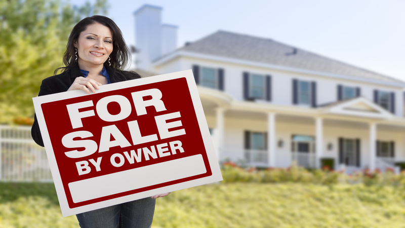 Smiling Hispanic Female Holding For Sale By Owner Sign In Front of Beautiful House.